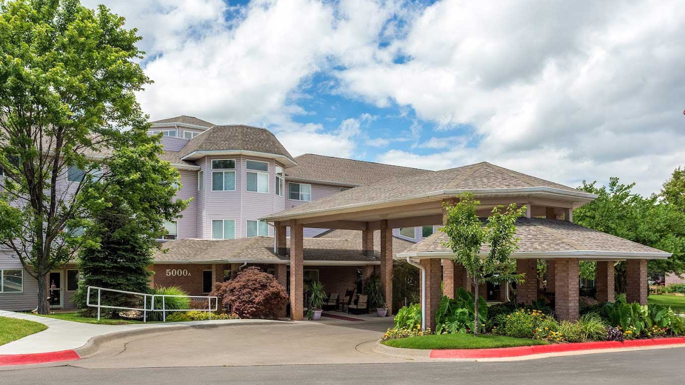 Front entrance of The Gardens at Arkanshire Senior Living, showcasing landscaped greenery and modern architecture.