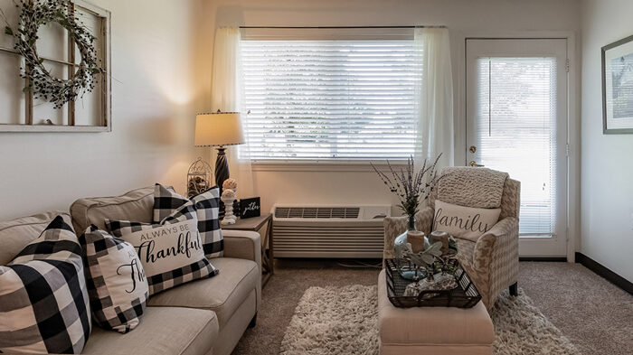 Cozy living room decorated with plaid pillows, a 'thankful' sign, and a wreath on the wall, creating a warm and inviting atmosphere.
