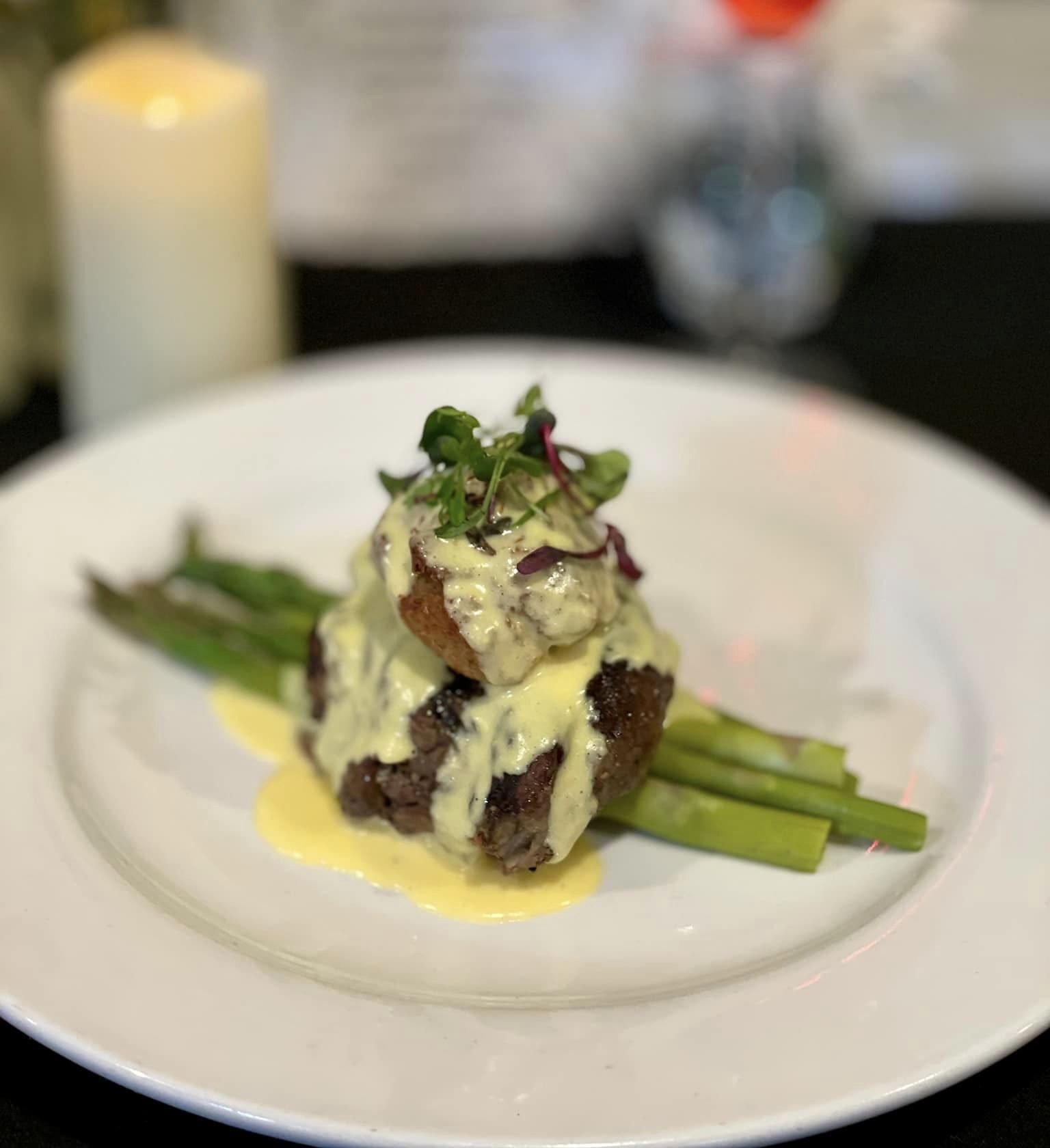 Close-up of a gourmet dish featuring crispy pork belly garnished with microgreens and accompanied by sautéed vegetables, presented on a plate with artistic sauce drizzles.