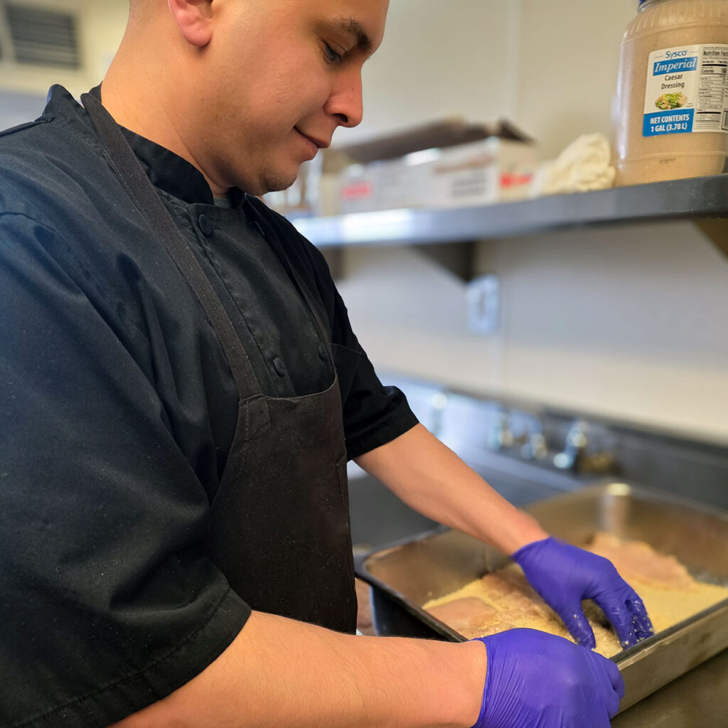 Culinary team member at The Gardens at Arkanshire Senior Living prepares a meal with fresh ingredients.