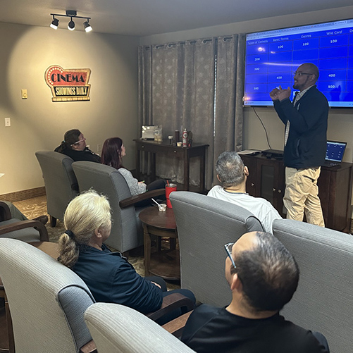 A team member at Gardens at Arkanshire Senior Living hosts a game of Jeopardy in the cinema room.