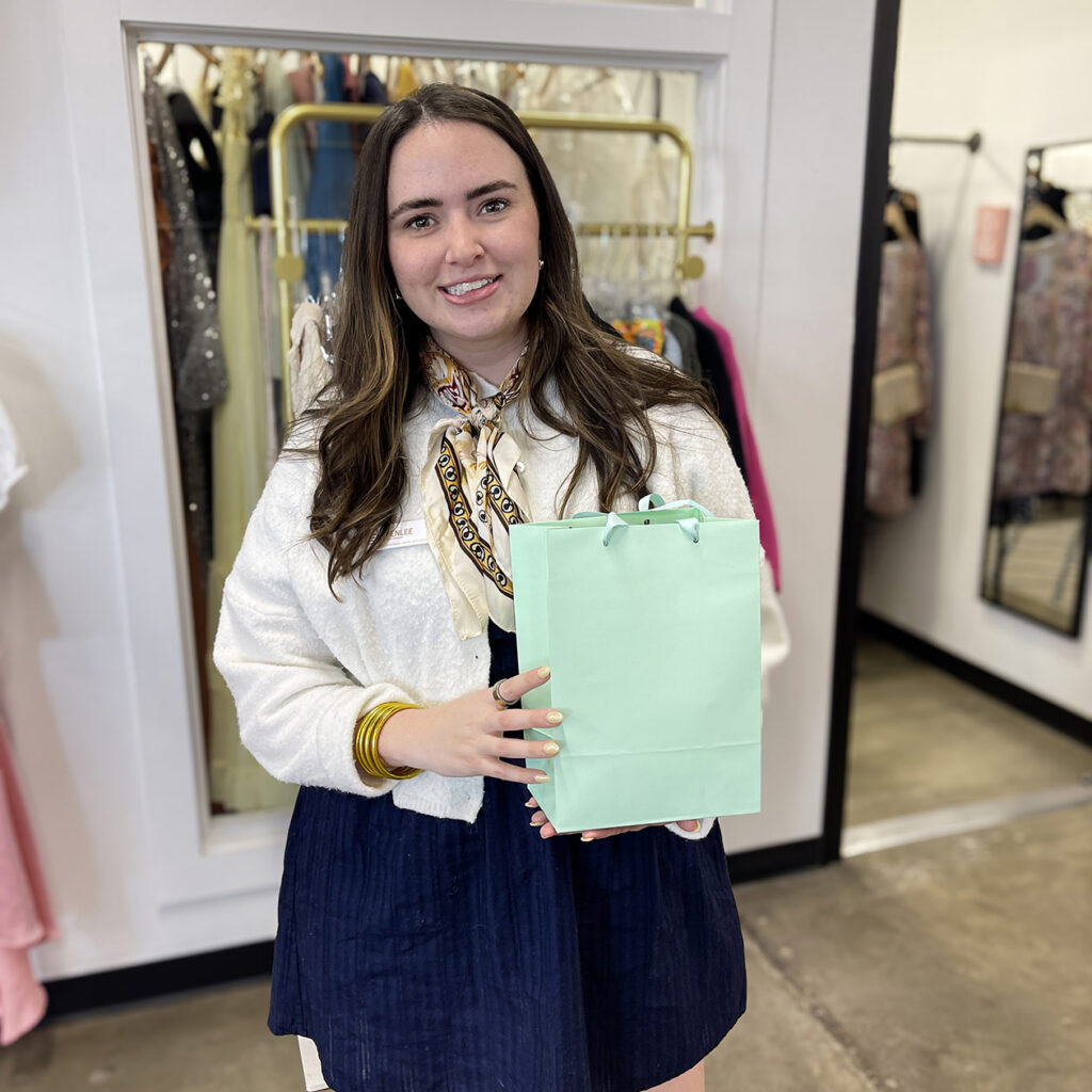 A woman from a local business smiles, holding a mint green gift bag.
