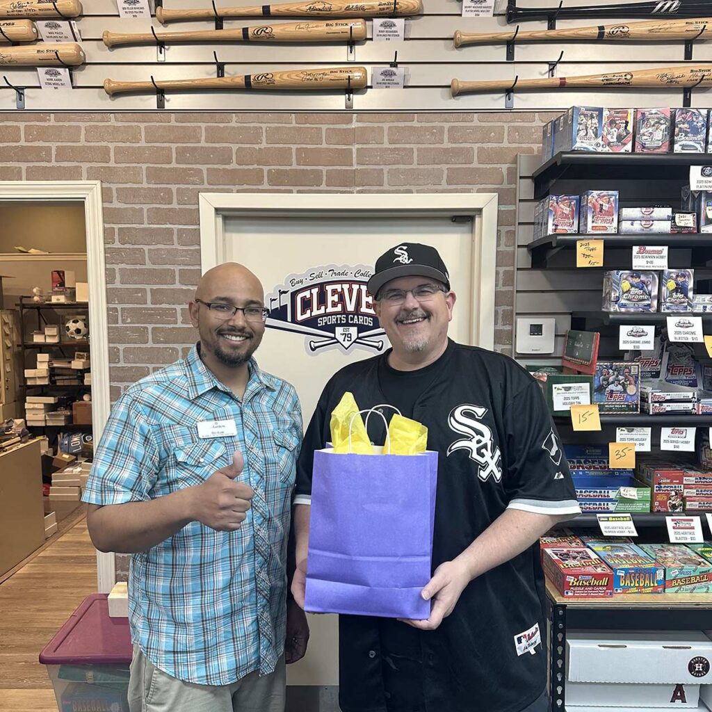A man from The Gardens at Arkanshire Senior Living presents a gift bag in thanks to a local owner of a sports cards business.