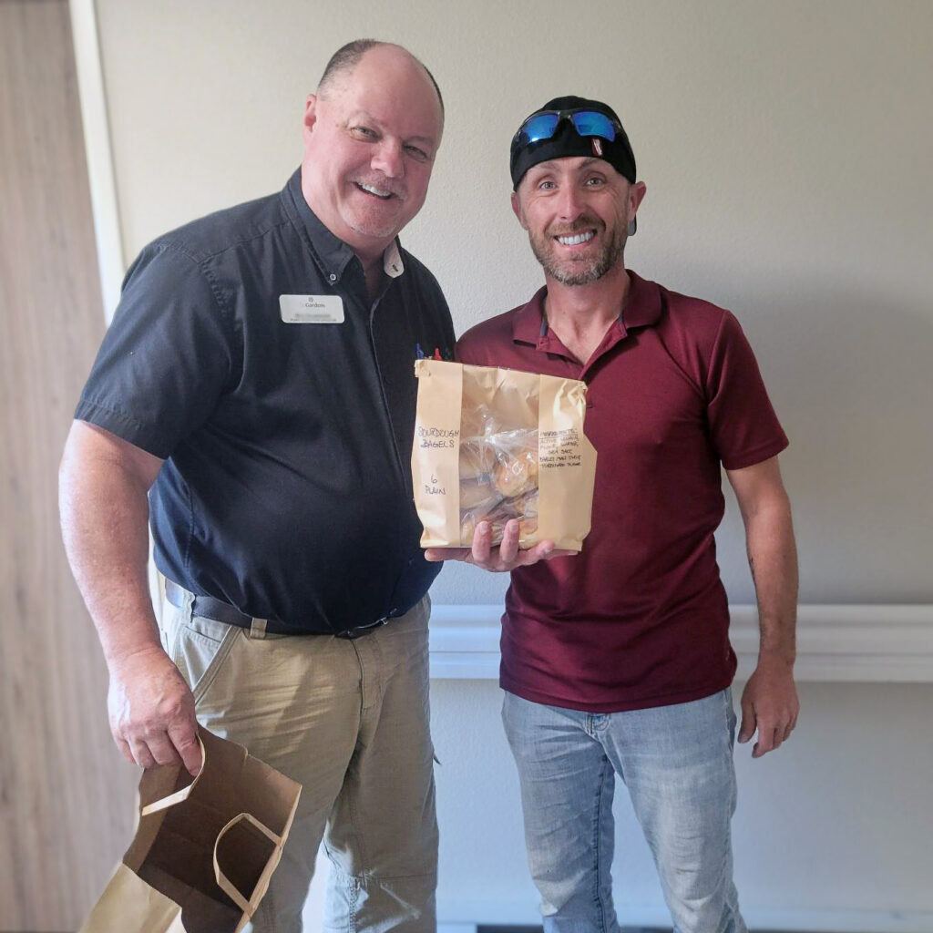 A man from The Gardens at Arkanshire smiles alongside a local business owner, presenting a gift bag.